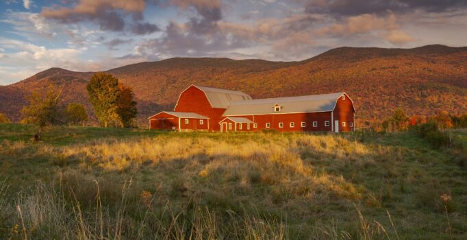 Red barn in a Vermont field with foliage colors in the background hills.