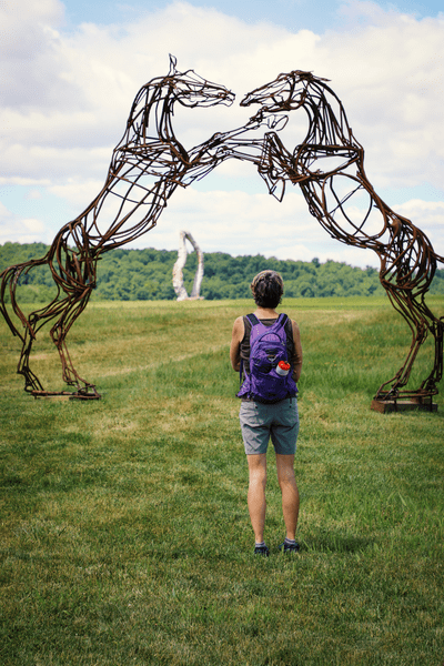 A person looking up at a sculpture of two horses rearing up on their back legs.