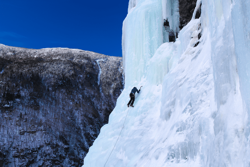 A person ice climbs the side of a mountain in winter.