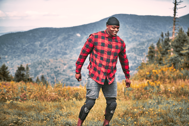 A person wearing red and black flannel walks through a field smiling.