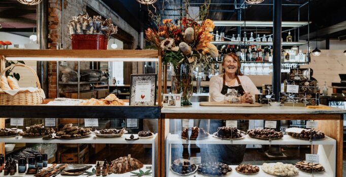 A person stands behind a shop counter with chocolates and other sweets on display.
