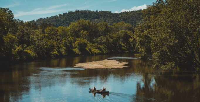 A couple canoe along a quiet river.