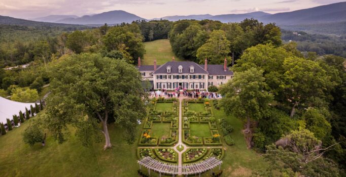 A historic mansion seen from above in the summer, nestled between mountains.