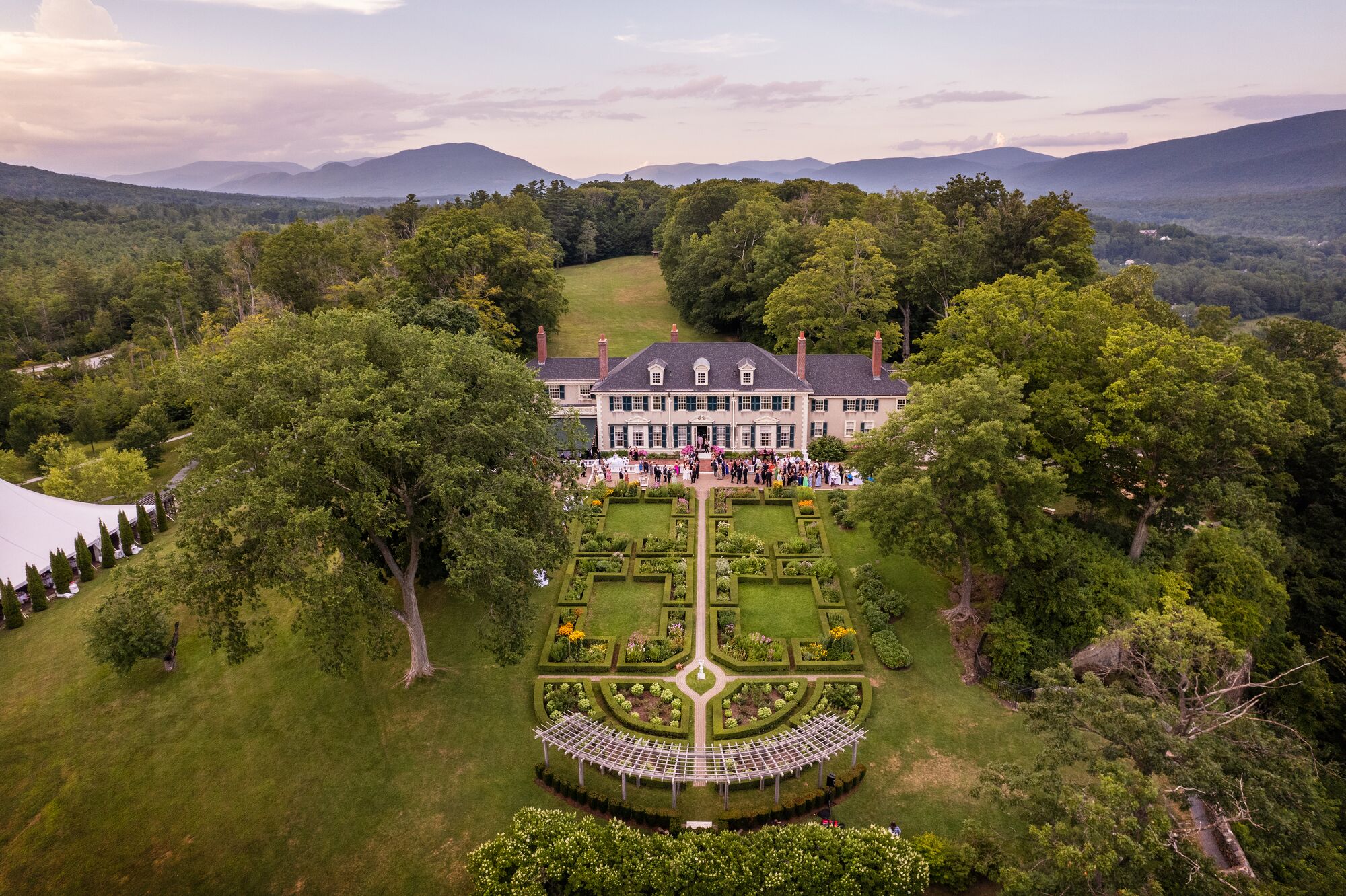 A historic mansion seen from above in the summer, nestled between mountains.