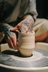 A person uses a pottery wheel to form clay with their hands.