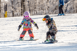 Two children slide down a ski trail on snowboards.