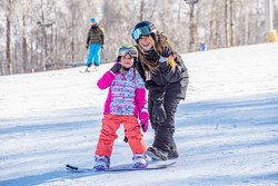 An adult and a child on skis and snowboards outdoors at a resort in the winter.