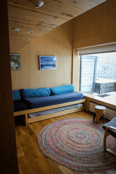 A room with wooden wall panels, a couch, area rug, and table by a window.