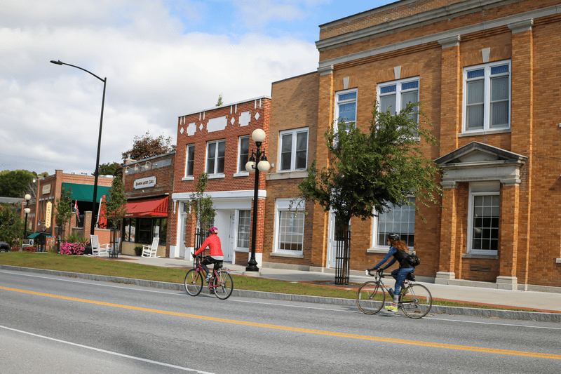 Two people ride bikes down a street lined with historic brick buildings.