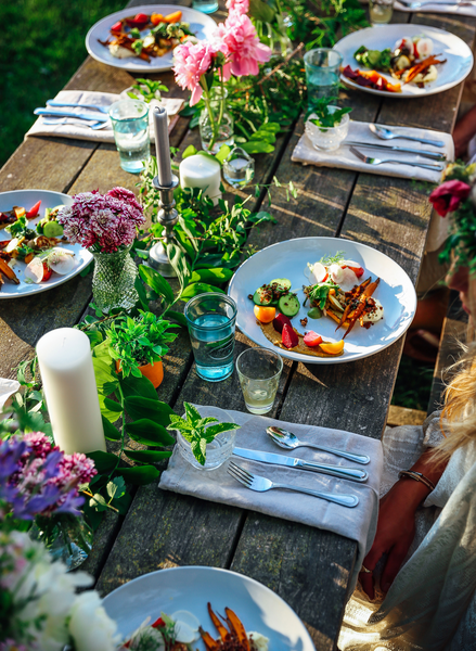 As seen from above, a group of place settings sit on a wooden table outdoors on a warm sunny day.