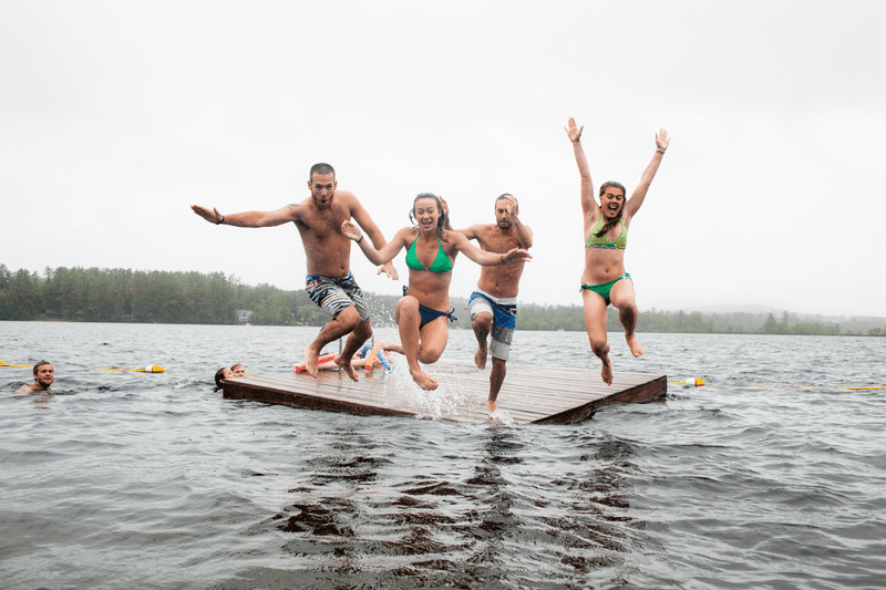 Four people midair after jumping off a dock on a lake.