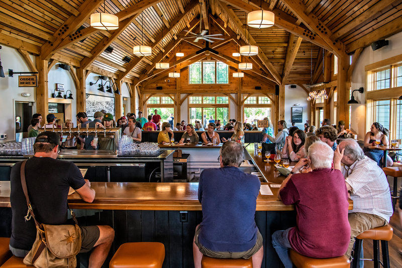 People sit in a brewery with timber framing in the ceiling and large windows.