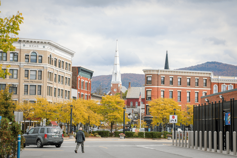 A downtown with historic brick buildings, a white church steeple, and mountains in the background.
