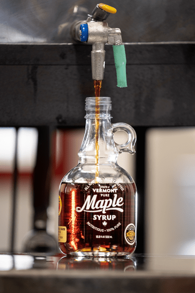 Maple syrup dispenses out of a tap into a glass jug.
