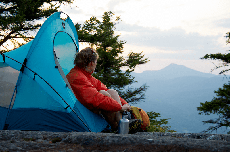 A person sits in an open tent looking at the view of a mountain.