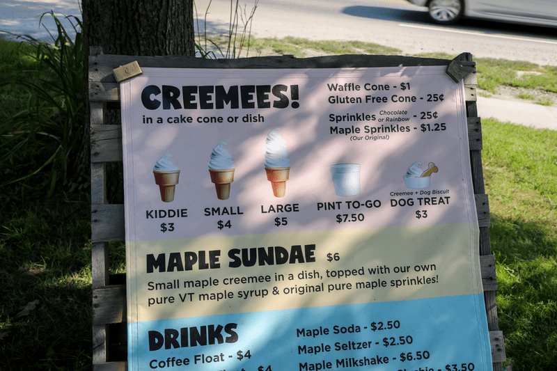 A sign advertising Creemees shows prices and sizes available for purchase outside on a sunny day.