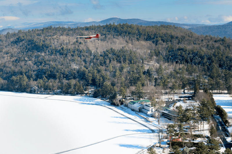 Seen from above, a frozen lake with a trail next to a snowy mountain in the winter.