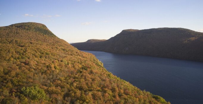An aerial view of Lake Willoughby in Vermont during the autumn peak, showcasing a vibrant canopy of red, orange, and yellow foliage framing the deep blue water.