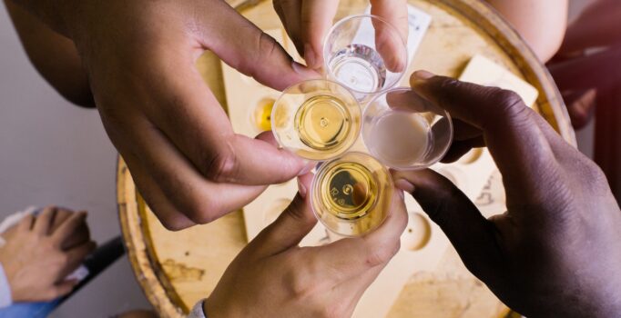 Seen from above, four hands are visible holding samples of liquors and toasting.