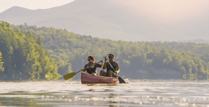 Two people paddle a canoe on a mountain lake on a warm day.