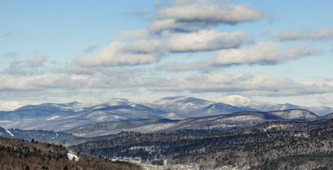 Seen from afar, snow-covered mountain peaks and a valley with a road running through it.