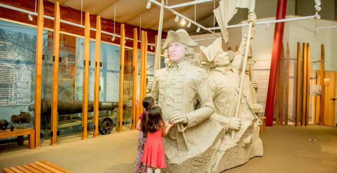 Two children stand in front of a large sculpture inside a museum.