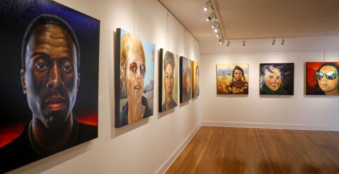 Multiple paintings hand on display on the walls of an art gallery.