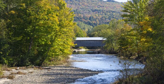 River flowing under a bridge with a mountain in the back with peak fall foliage.