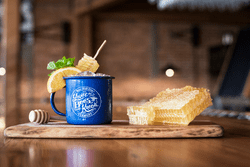 A cocktail in a blue mug on a wooden plank with a raw honeycomb beside.