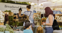 People purchase produce from farm's booth at a farmer's market