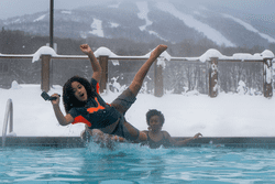 A person is seen jumping into a heated outdoor pool in the winter.