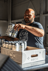 A person loads 4-packs of canned beer into a box.