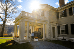 People gather to walk inside a beautifully restored 1900s mansion on a sunny day.