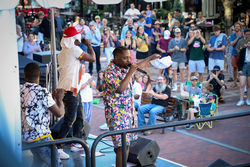A person in colorful clothes stands amid a crowd in an outdoor concert, singing.