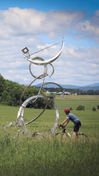 A person bikes by a large abstract metal sculpture.