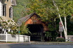 A covered bridge in a downtown tucked behind trees just starting to turn fall colors.