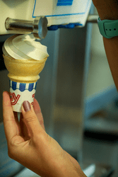 A close-up of a person swirling soft ice cream from a machine into a cone.