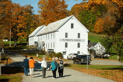 A fall scene with people gathering outside a white building with a sign that says Plymouth Cheese Company.