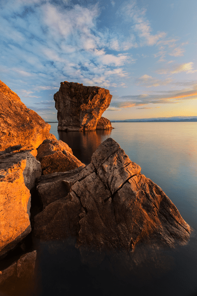 Large rock outcroppings jut out of a large body of water at sunrise.