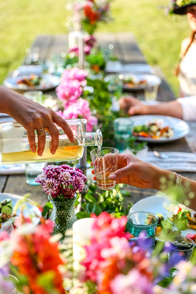Colorful arranged flowers ornament a table outdoors while hands pour glasses.