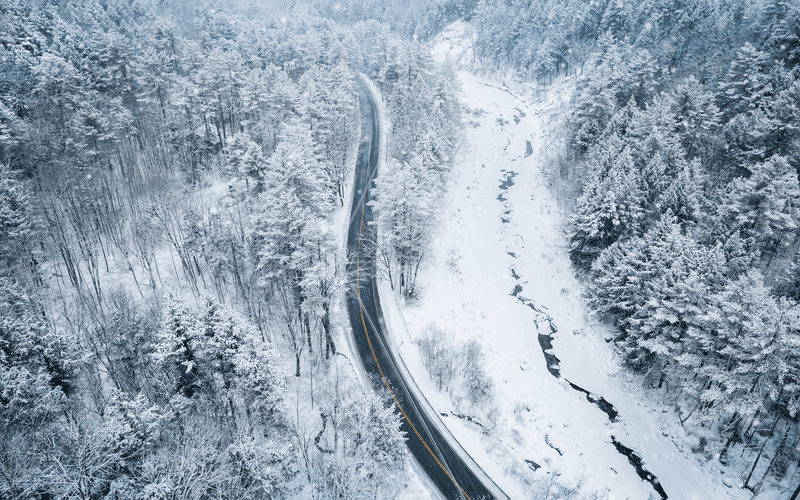 A car drives along a snowy winter road seen from above.