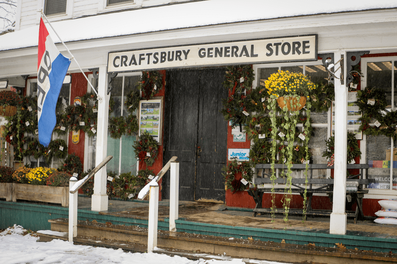 A white general store with a sign reading “Craftsbury General Store” seen from outside in the winter.