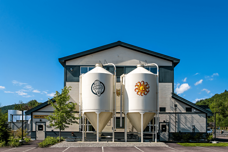 The exterior of a brewery is visible with two storage tanks on a sunny day.