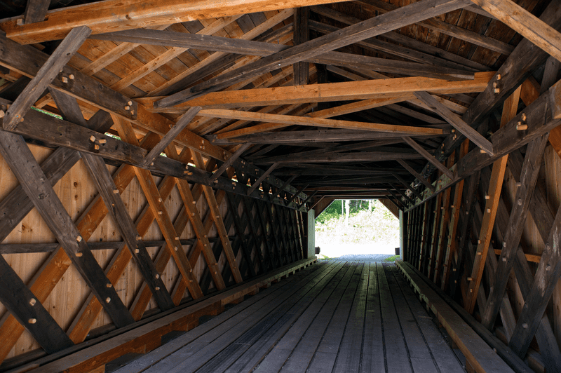 The inside of a covered bridge with light visible at the end.