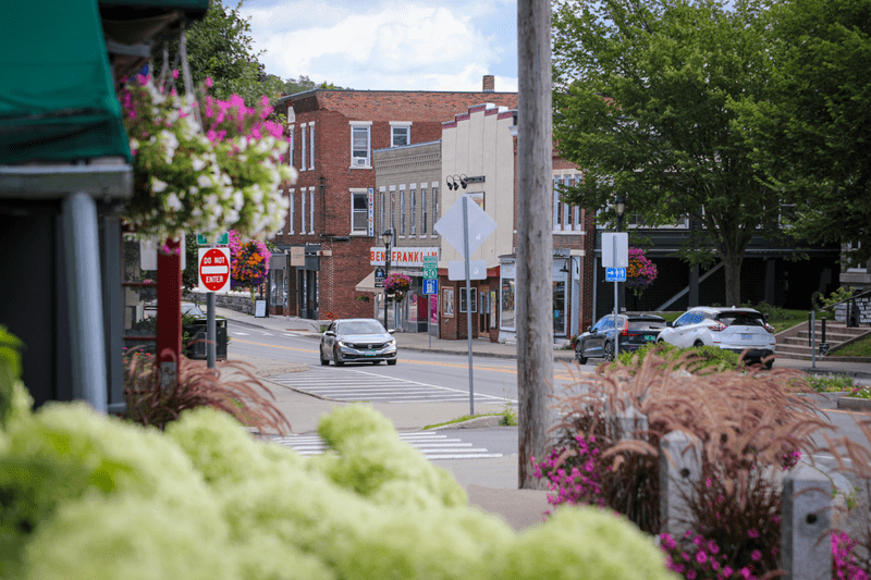A car drives through a historic downtown in the summer toward the camera.