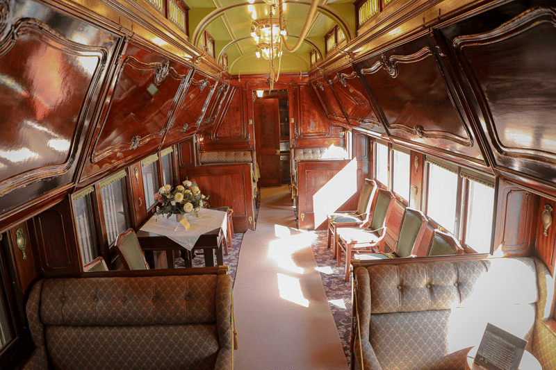 The plush interior of an antique Pullman train car, with dark wood framing and velvet seats.