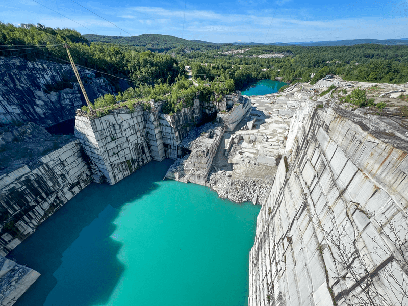 Bright blue water at the base of a granite quarry with white walls in the summer. 