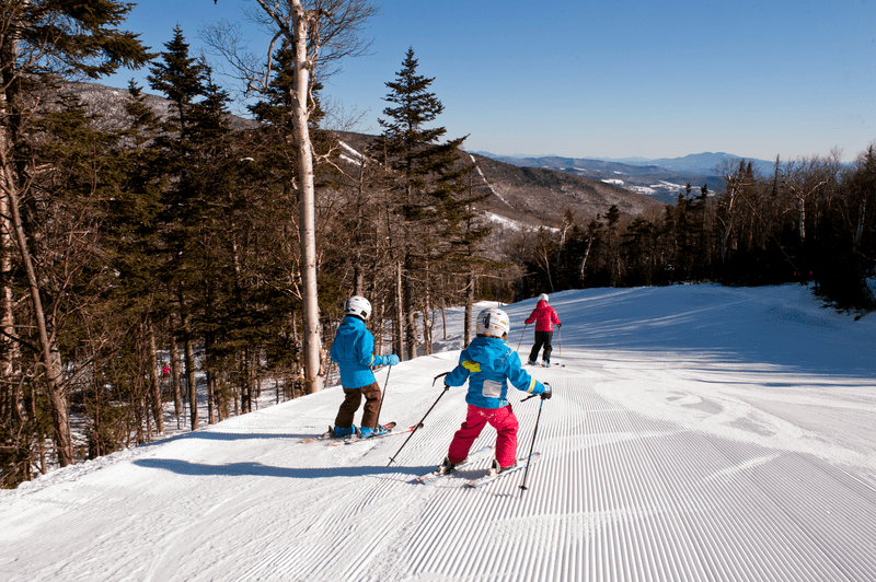 Three people ski down a groomed ski trail.