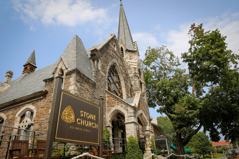 A grey stone church with a sign in front reading Stone Church.