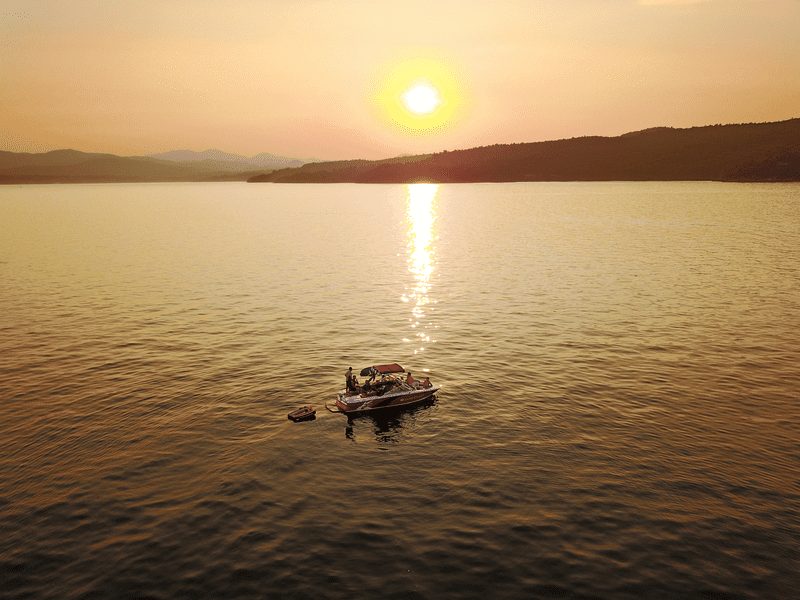 Seen from above, the sun reflects warm light on a lake and a floating boat.